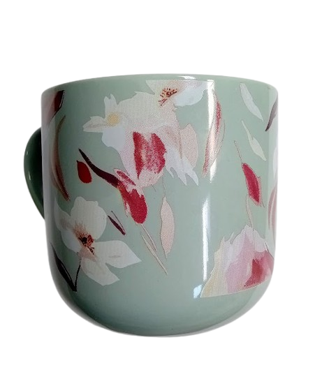 A green ceramic mug with a floral pattern of pink and white flowers and leaves.